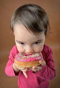 小女孩吃甜甜圈釉面微笑享受孩子们时间粉色蛋糕垃圾糖果婴儿图片