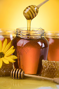 蜂蜜和木棍子放在桌子上营养玻璃金子国家糖浆花蜜蜂蜜瓶子石匠蜂巢背景图片