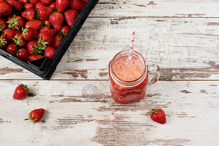 新鲜果汁 奶昔 草莓奶昔放在带吸管的梅森罐子里 一堆多汁的成熟有机新鲜草莓放在黑色的板条箱里 草莓鲜饮 淡淡的仿古木背景图片