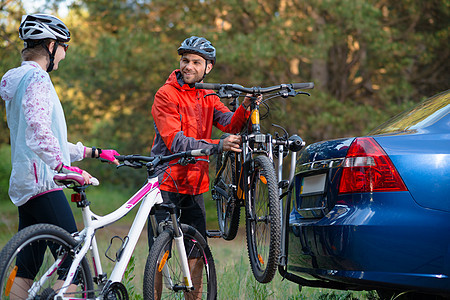 冒险与家庭旅行概念 由Bike Rack在汽车上搭乘的  年轻夫妇脱身山车蓝色松树女性载体站立运动森林安装头盔男人背景图片