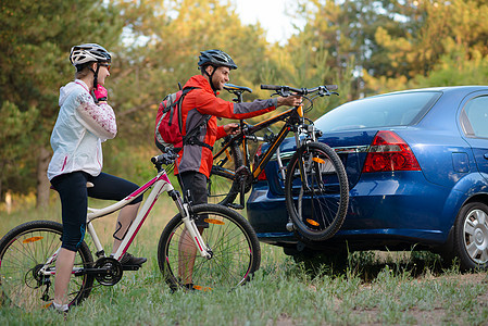 冒险与家庭旅行概念 由Bike Rack在汽车上搭乘的  年轻夫妇脱身山车蓝色运动森林耐力赛安装车辆头盔夫妻娱乐站立图片