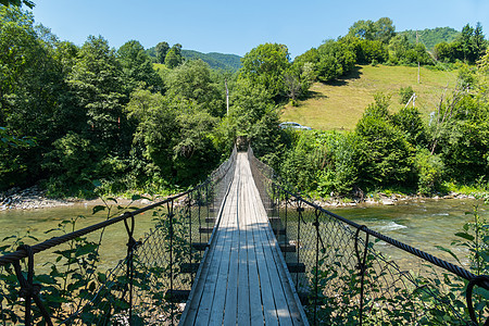 山地地区一条河对面铺设了一座人行桥 上面铺有木制吊带 另一边是一辆汽车图片