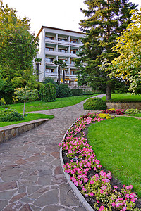 一条种有鲜花 高大绿树和草坪的石板路通向一栋带阳台的白色五层建筑 休息的地方 旅馆 旅馆 疗养院图片