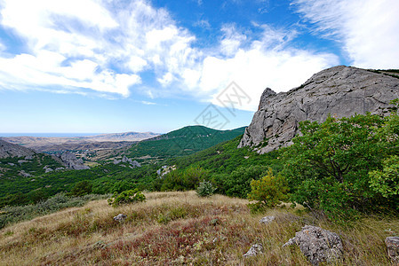 一片岩石状山峰和绿山的风景 其背景是白云模糊的苍蓝天空图片