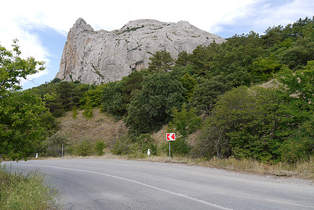 一条陡峭的公路在绿色植被和高岩山的背景下转弯而起图片