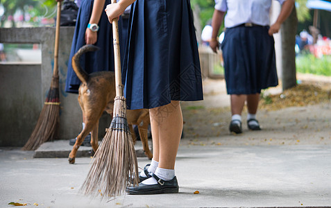 女学生帮助在狗走路时用扫帚扫清混凝土地板图片