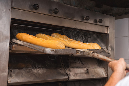 贝克从工业烤箱里拿出新鲜面包面包面团成人工作服火炉小麦职场工厂烹饪职业产品图片