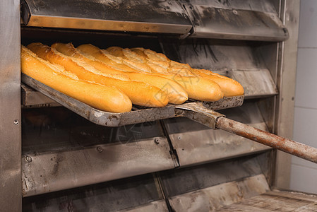 贝克从工业烤箱里拿出新鲜面包面包食物机械工人男人质量糕点食品面粉小麦工作服图片