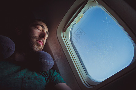 长着脖子枕头的年轻人休息和睡在飞机上图片