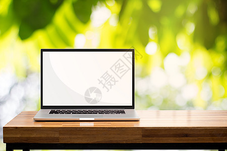 绿色花园中木制桌上的笔记本电脑空白屏幕图片