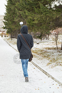 一个穿着夹克和兜帽的年轻人 快速骑在通往冬季公园的雪盖路上图片