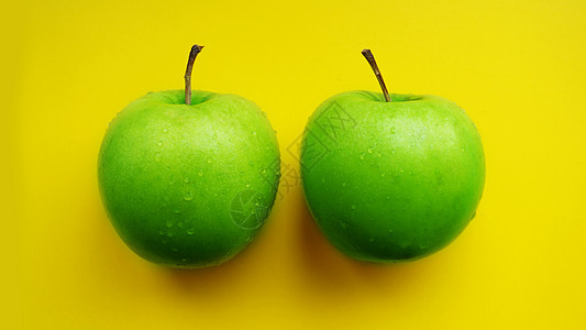 水滴中的绿苹果 - 黄色背景孤立于密闭的宏顶视图图片