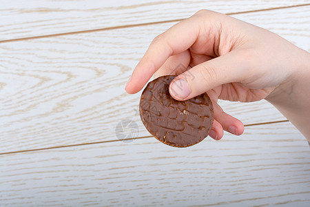 手握着一个巧克力 覆盖的饼干 在木制背景涂层食物糖果棕色小吃甜点圆形蛋糕白色木头图片