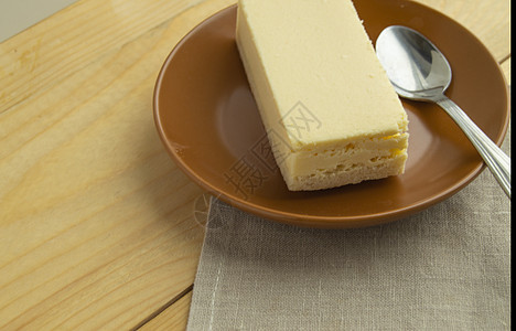 一块香草芝士蛋糕 躺在棕色的盘子上 浅木本底和纸巾图片