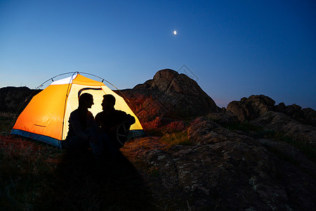 坐在月亮上在山边的博蒂鲁尔晚宴上坐着 坐在不光化帐篷附近 互相看着对方男人假期夫妻自由旅游女性日落天空蓝色橙子背景