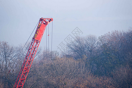 建筑工序 建造有红色刺青的汽车起重机 秋雾和背景模糊的河桥 起重机周围的森林蓝色街道绞刑架电梯机器警告安全建筑建筑学城市图片