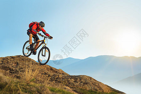 红色骑车的赛车运动员 在日出时在岩石下沉 极端运动和概念爬坡山地车男性头盔活动自行车耐力赛娱乐下坡金子图片