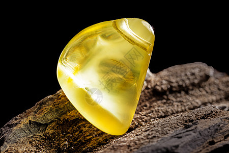 天然琥珀 黄色不透明的天然琥珀 在大片黑石头木头上黄油分层蜂蜜抛光反射珠子化石裂缝材料琥珀色图片