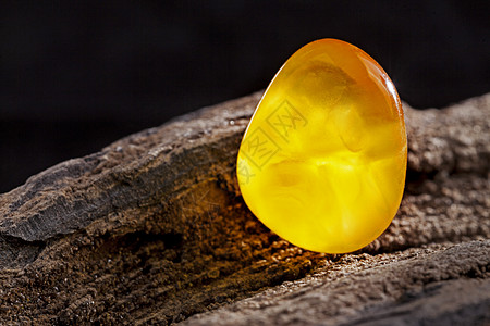 天然琥珀 黄色不透明的天然琥珀 在大片黑石头木头上太阳石珠子反射矿物材料黄油宝石琥珀色珠宝抛光图片