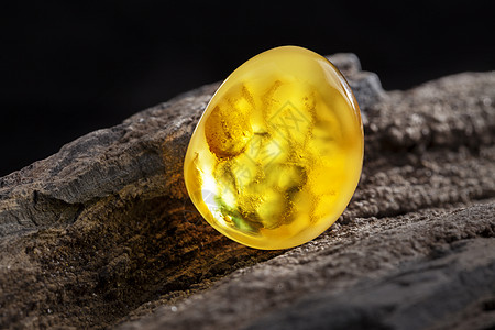 天然琥珀 黄色不透明的天然琥珀 在大片黑石头木头上蜂蜜珠子分层反射材料矿物宏观裂缝黄油珠宝图片