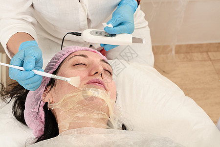 美容仪器在美容院的年轻女子 做超声波剥皮 和面部清洗程序女士硬件除垢仪器机器电疗诊所美容按摩护理背景