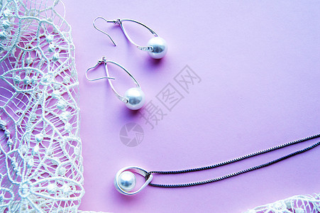 漂亮的银色闪亮珍珠首饰 带有时尚的霓虹灯 时尚迷人的耳环 粉色紫色背景上的链条和精致的蕾丝 平躺图片