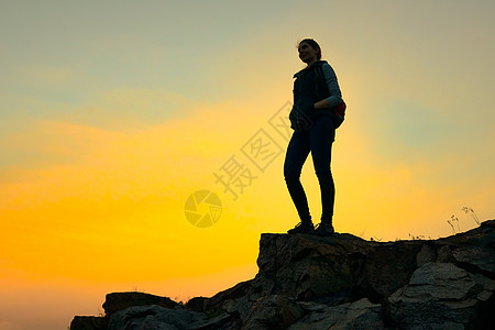 女士手表年轻女旅行家和背包在夏日日落的岩石顶端站着 旅行与冒险概念自由远足者手表女士远足游客女孩爬坡站立晴天背景