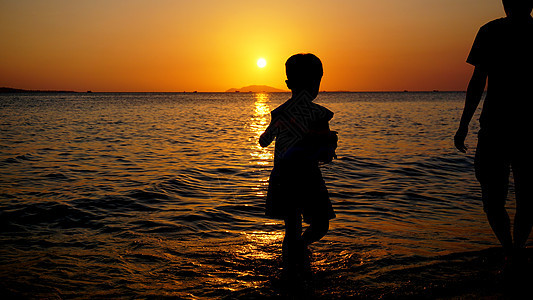 父亲和孩子在日落时在海滩玩耍 家庭概念图片