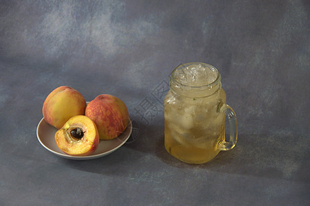 半颗桃子 整块半在陶瓷圆盘上 一杯杯子里有果汁和冰 在灰色的抽象背景上图片