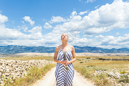 夏季 身着夏装的白人年轻女性手持薰衣草花束 在帕格岛多岩石的克罗地亚海岸景观中享受纯地中海的自然风光女孩快乐福利自由旅游条纹闲暇图片