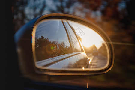汽车侧面镜子中阳光模糊 反射在日落的阳光下的道路交通窗户沥青太阳橙子蓝色车辆玻璃运动天空图片