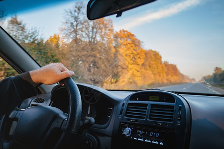 一名男子驾驶一辆汽车在秋天的黄橙黄色路上行驶女士公园旅行女性方向盘地平线天空环境窗户世界图片