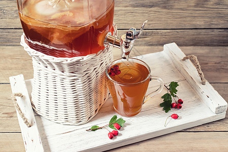在有水龙头的罐子中和在白盘上的一个杯子里用木质背景的胡须浆果来装发酵茶饮图片