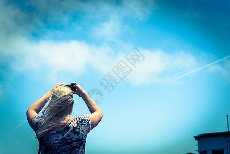 带横体袋的白金金金发女人 从手机上拍到蓝色天空的照片图片