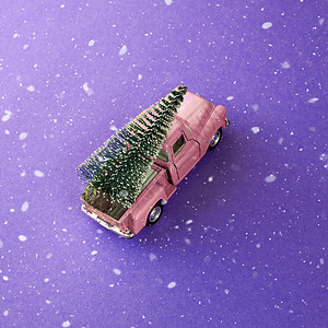 一辆微型粉红色汽车在后面载着一棵圣诞树 在简单的紫色背景下 雪下 顶视图 节省空间 概念 节日的圣诞气氛 送礼 趋势图片