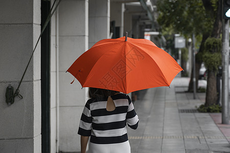 背对着女人的眼神 带着橙色雨伞在街上行走天气沉思女士街道季节成人外套下雨乐趣生活图片