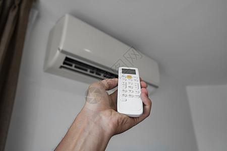 使用遥控器的人的手 手持 rc 和调节安装在白墙上的空调温度 室内舒适温度 健康理念和节能控制办公室手臂状况净化器器具房间气候按图片