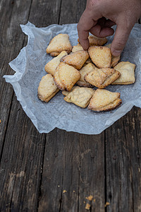 男人的手抓着卷曲饼和三角饼干 在白纸上 在古老的黑木木背景上身体味道面包师午餐麻布沙漠草本植物烘烤女性手指图片
