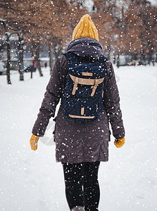 快乐的年轻欧洲女人戴着黄色针织帽 戴着手套 背着背包 在大雪中笑着离开 从后面看 复古效果 模糊雪花喜悦降雪头发青年自由享受微笑图片