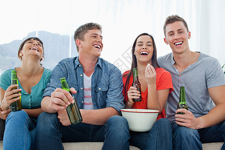 一群欢笑的朋友们坐在他们手里拿着啤酒喝着啤酒 吃爆米花图片
