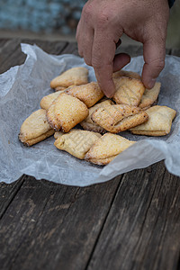 男人的手抓着卷曲饼和三角饼干 在白纸上 在古老的黑木木背景上麻布蜂蜜身体烤箱草本植物高架手指烘烤菜单面包师图片