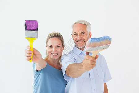 幸福的情侣拿着画笔微笑着镜头紫色蓝色服装家装感情男性衬衫浅色夫妻快乐图片
