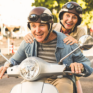 快乐的成熟情侣在城里骑摩托车驾驶晴天退休车辆乐趣活动男性金发微笑骑术图片