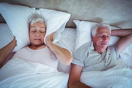 年长妇女用枕头挡耳朵 而丈夫在床上打呼噜图片