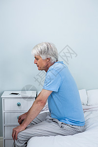 深思熟虑的老人坐在床上的侧面观图片