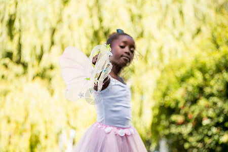 穿着童话服 用魔杖对着相机的可爱混合种族女孩黑发公主幸福手指阳光绿地公园童年魔法棒乐趣背景图片