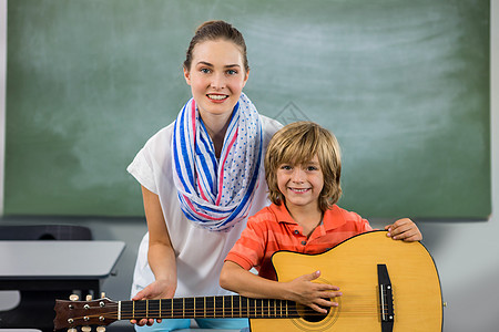 年轻老师协助男孩弹吉他的肖像图片