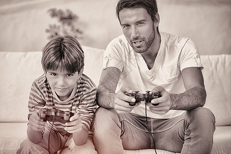 父亲和儿子玩电子游戏控制器快乐家庭男人长椅视频男性孩子客厅牙裔图片