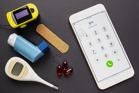 手机银行卡智能手机呼叫911拨号紧急服务 配有哮喘吸入器 绷带 一些药片和黑色的血氧计背景