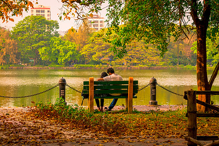 年轻夫妇坐在湖岸的秋天公园长椅上 爱上了Mamele树叶花园 放松和浪漫活动被大自然中的美人包围着日落摄影森林假期田园树冠草地两图片